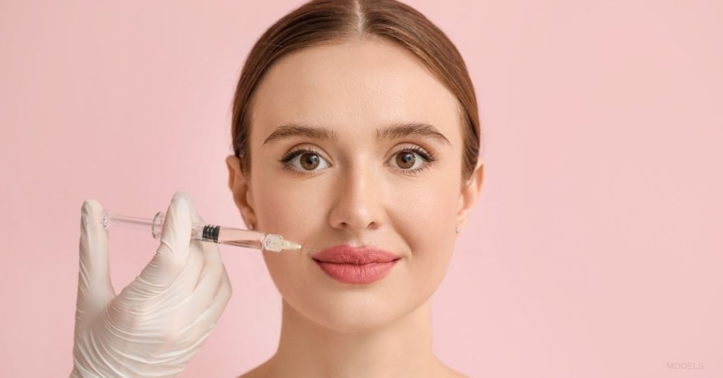 Woman facing straight forward smiling while getting dermal fillers (MODELS)